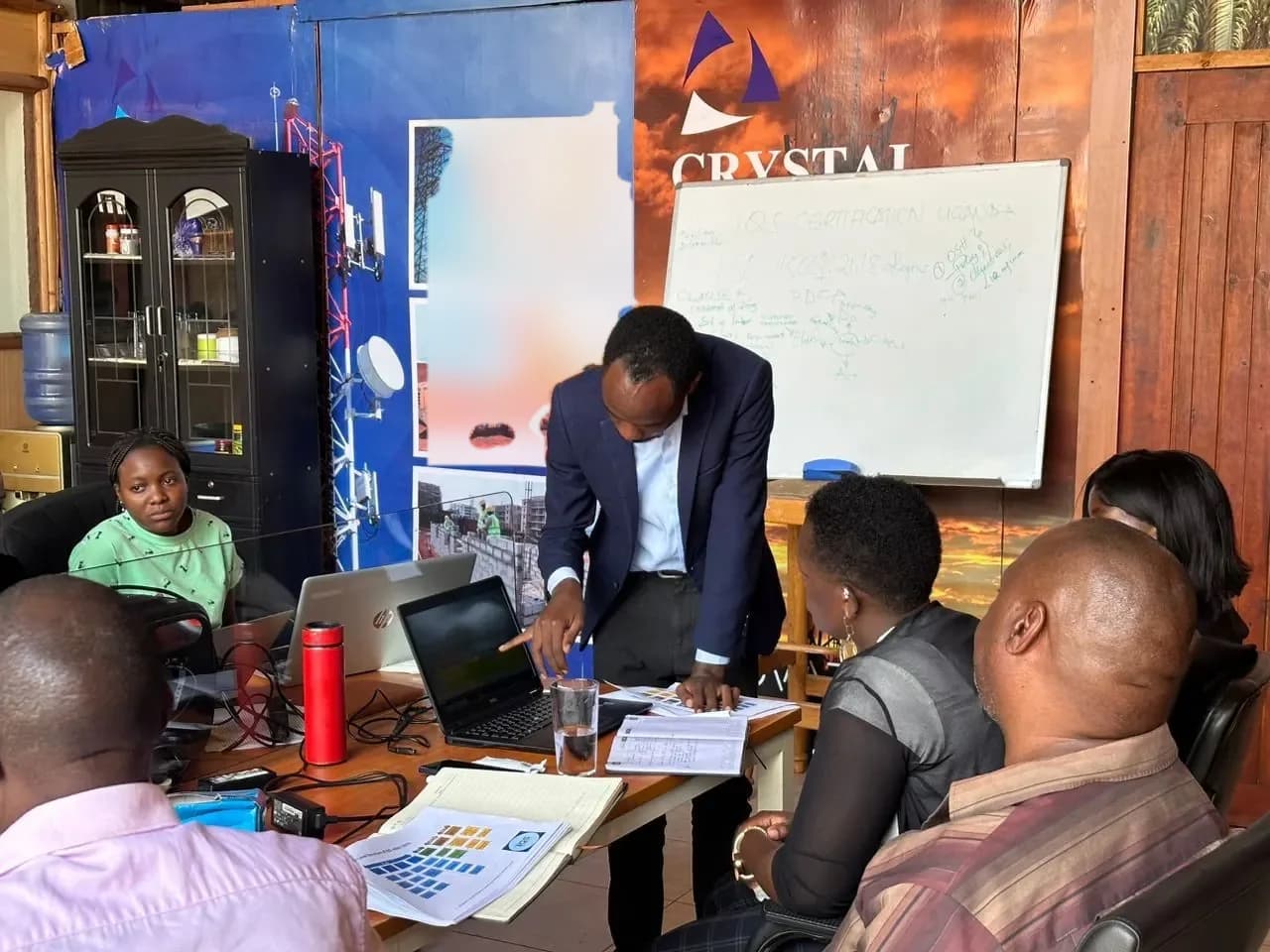 A trainer pointing at a whiteboard of diagrams while professionals seated at a conference table take notes